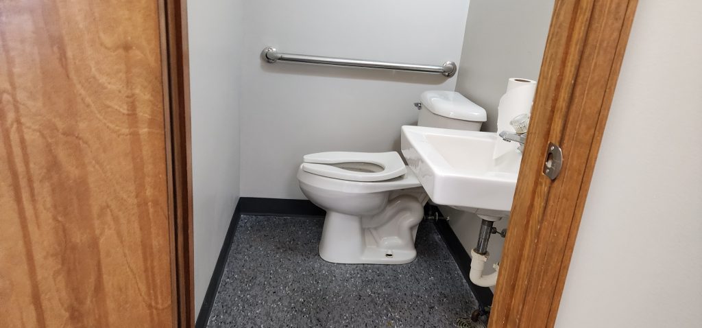 Small bathroom with a white toilet and a wall-mounted sink, a metal grab bar on the wall, and a roll of paper towels on the sink.